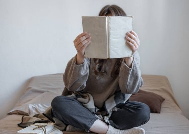 Genç kadın yatakta otururken bir kitap okuyor..