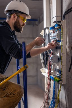 Bir erkek elektrikçi elektrik kablosuyla santralde çalışıyor..