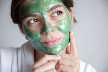 Yüzünde yeşil kozmetik maske olan çekici genç bir kadın..