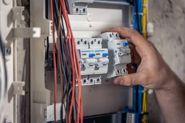 Um eletricista masculino trabalha em um quadro com um cabo de conexão elétrica . — Fotografia de Stock