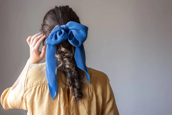 Visão traseira, uma menina em um vestido com um arco no cabelo em um fundo cinza. — Fotografia de Stock