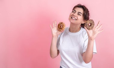 Güzel, genç bir kadının portresi pembe arka planda izole edilmiş çörekleri gösteriyor..