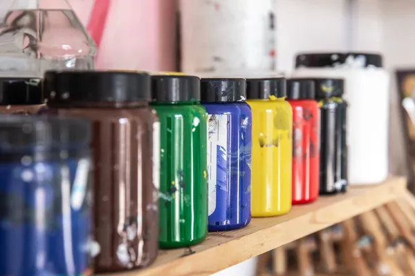 Colored paints for drawing and painting in cans on a shelf in a workshop. — Stock Photo, Image