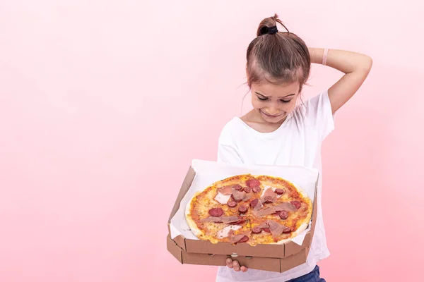 Menina engraçada com pizza em uma caixa em um fundo rosa, espaço de cópia. — Fotografia de Stock