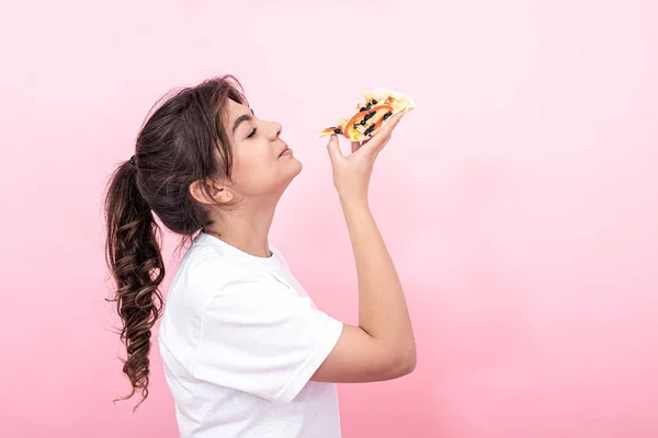 Приваблива дівчина з шматочком піци на рожевому фоні, копіювати простір . — стокове фото