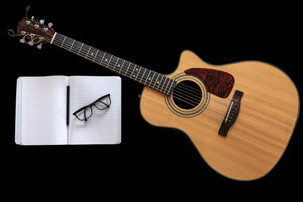 Guitarra acústica clássica e um caderno aberto sobre fundo preto. — Fotografia de Stock