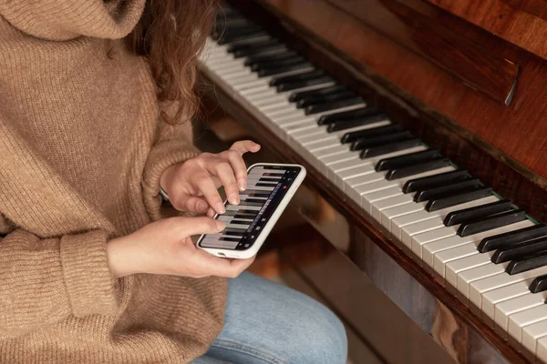 Женщина учится играть на пианино с помощью приложения на телефоне. — стоковое фото