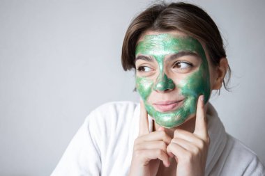 Yüzünde yeşil kozmetik maske olan çekici genç bir kadın..
