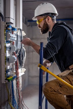 Bir erkek elektrikçi elektrik kablosuyla santralde çalışıyor..