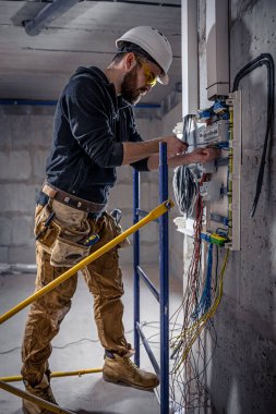 Bir erkek elektrikçi elektrik kablosuyla santralde çalışıyor..