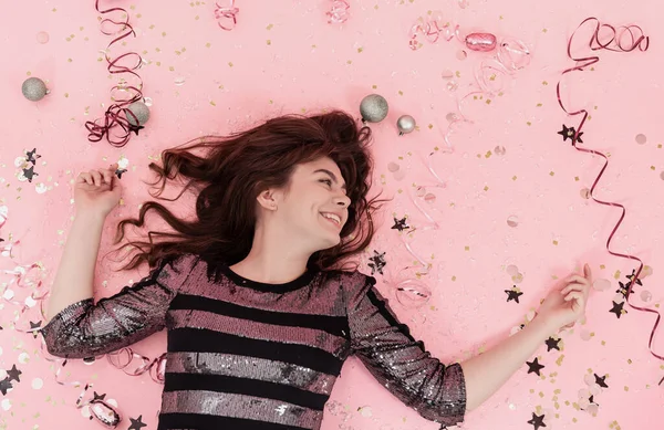 快乐的女孩躺在粉红的背景上，在五彩纸屑和蛇纹石之间，尽收眼底. — 图库照片