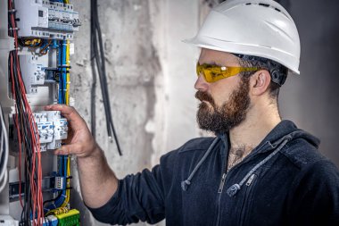 Bir erkek elektrikçi elektrik kablosuyla santralde çalışıyor..