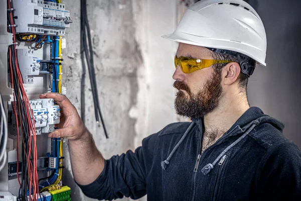 オスの電気技師は電気接続ケーブルのあるスイッチボードで働いています. — ストック写真