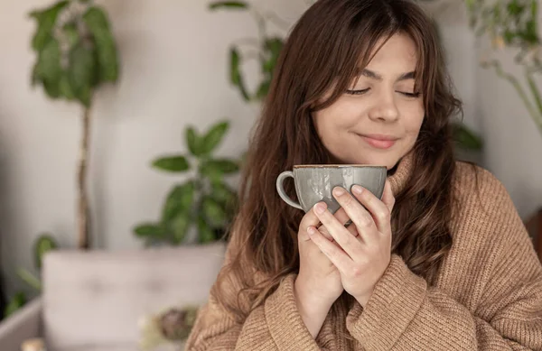 Молодая женщина в уютном свитере наслаждается чашечкой напитка. — стоковое фото