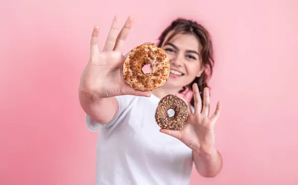 Güzel, genç bir kadının portresi pembe arka planda izole edilmiş çörekleri gösteriyor.. — Stok fotoğraf