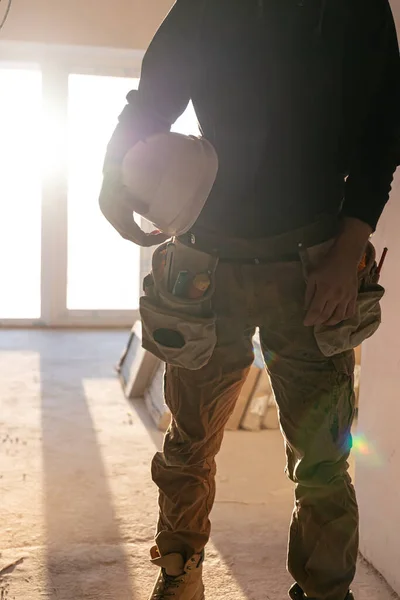 A man builder holds a protective helmet in his hands, part of the body. — Stock Photo, Image