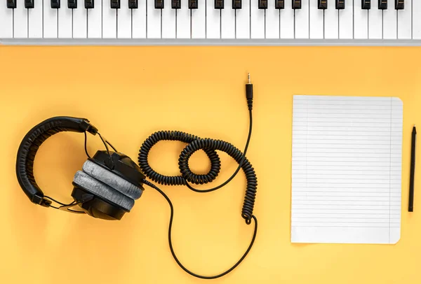 Headphones, musical keys and a blank sheet of paper on a yellow background. — Stock Photo, Image