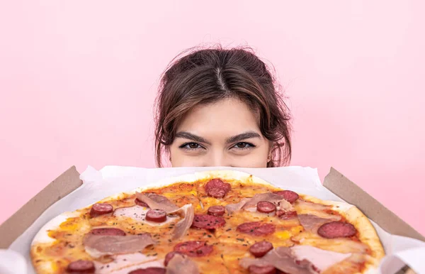 Menina atraente segurando pizza em uma caixa de papelão em um fundo rosa. — Fotografia de Stock