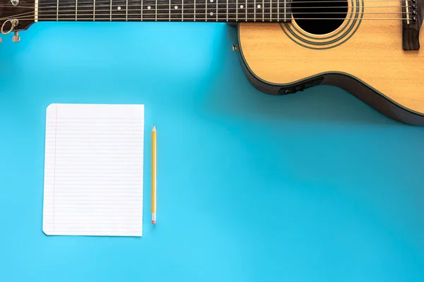 Akustisk gitarr och tomt papper på blå bakgrund, ovanifrån. — Stockfoto
