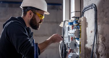 Bir erkek elektrikçi elektrik kablosuyla santralde çalışıyor..
