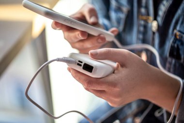 Bir kadının elinde bir güç bankası ve elinde bir telefon var..