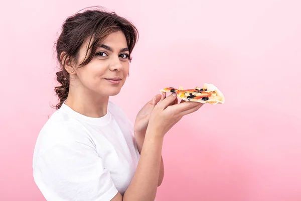 Приваблива дівчина з шматочком піци на рожевому фоні, копіювати простір . — стокове фото