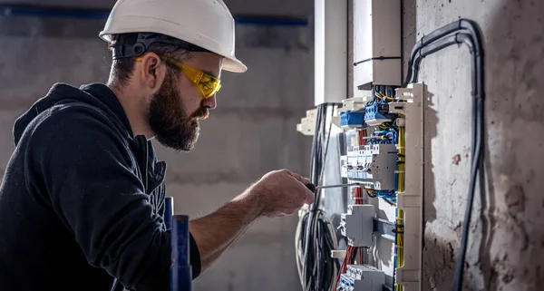 Bir erkek elektrikçi elektrik kablosuyla santralde çalışıyor..