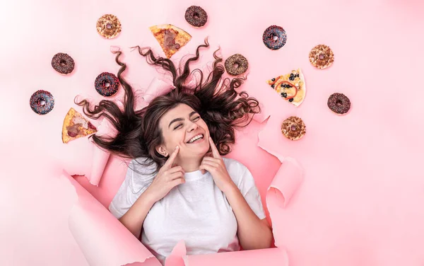 Pembe arka planda pizza ve çöreklerle çekici genç bir kadın.. — Stok fotoğraf