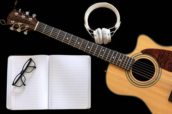 Klassisk akustisk gitarr, hörlurar och anteckningsbok på svart bakgrund. — Stockfoto