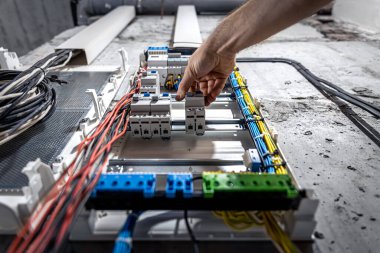 Bir erkek elektrikçi elektrik kablosuyla santralde çalışıyor..