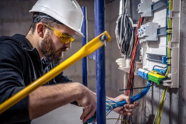 Bir erkek elektrikçi elektrik kablosuyla santralde çalışıyor..