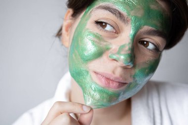 Yüzünde yeşil kozmetik maske olan çekici genç bir kadın..