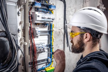 Bir erkek elektrikçi elektrik kablosuyla santralde çalışıyor..