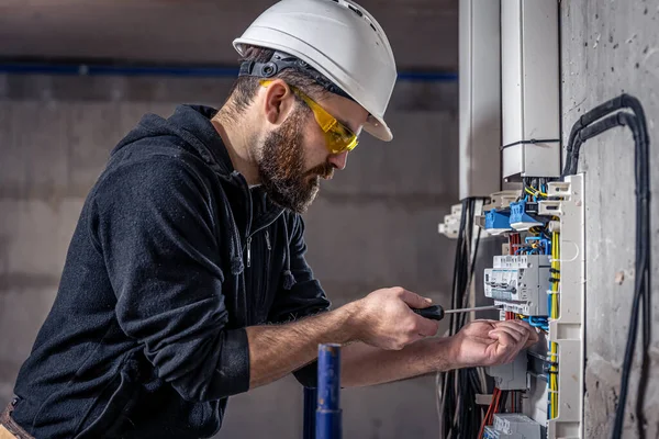 Een mannelijke elektricien werkt in een schakelbord met een elektrische aansluitkabel. — Stockfoto
