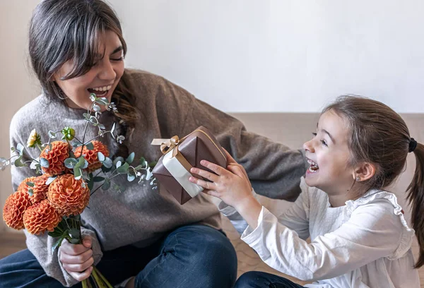 Маленькая девочка дарит своей матери подарок и букет цветов. — стоковое фото
