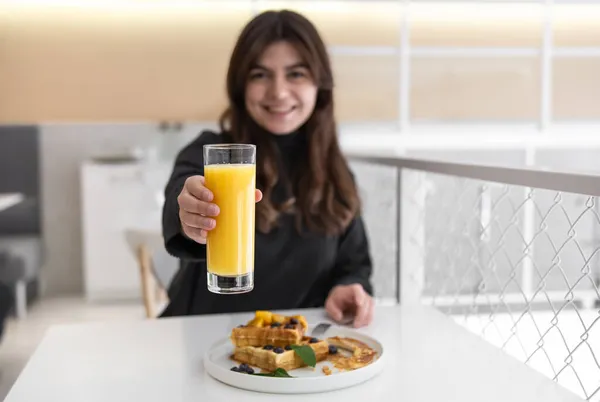 Una mujer está desayunando con gofres belgas y zumo de naranja. — Foto de Stock