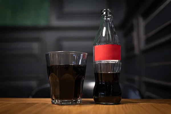 Close-up de uma garrafa de vidro com um rótulo vermelho e um copo de bebida carbonatada. — Fotografia de Stock