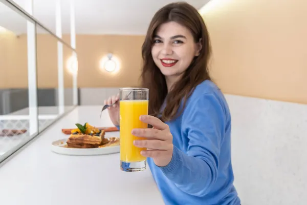 Atractiva joven come gofres belgas y jugo para el desayuno. — Foto de Stock