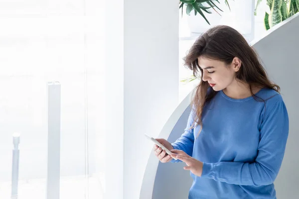 Mujer joven atractiva en un suéter azul utiliza el teléfono, espacio de copia. — Foto de Stock