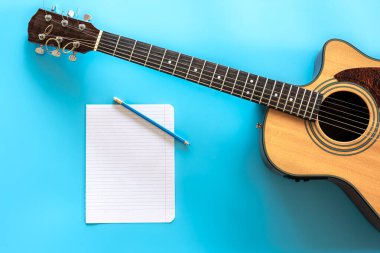 Akustik gitar ve mavi arkaplan üzerine boş kağıt, üst görünüm.