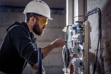 Bir erkek elektrikçi elektrik kablosuyla santralde çalışıyor..