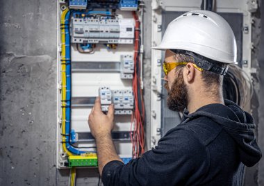 Bir erkek elektrikçi elektrik kablosuyla santralde çalışıyor..