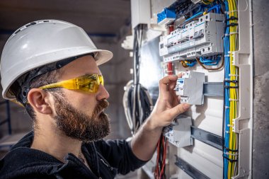 Bir erkek elektrikçi elektrik kablosuyla santralde çalışıyor..