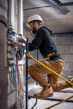 Bir erkek elektrikçi elektrik kablosuyla santralde çalışıyor..