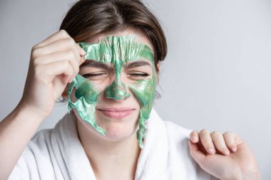 Çekici kız yüzünden yeşil bir kozmetik maske çıkarıyorum..