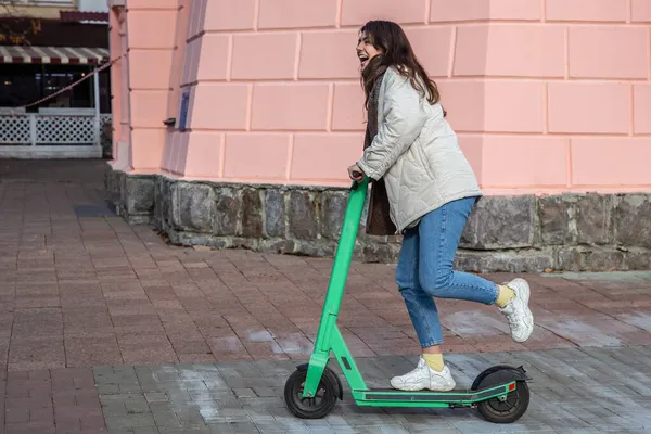 Şehirde elektrikli scooter kullanan mutlu genç bir kadın..