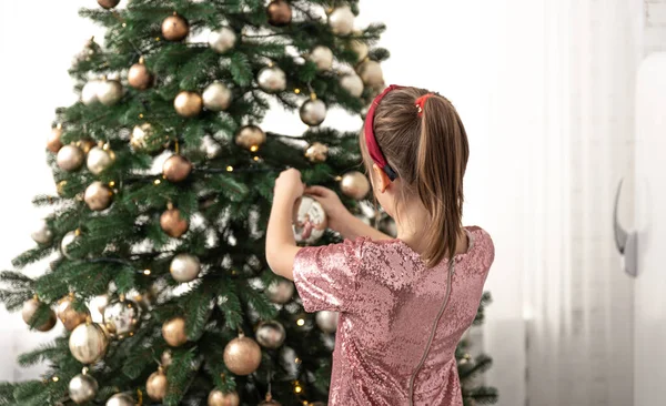 Una niña pequeña decora un árbol de Navidad, cuelga bolas. Imágenes De Stock Sin Royalties Gratis