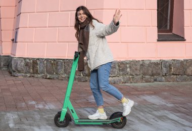 Şehirde elektrikli scooter kullanan mutlu genç bir kadın..