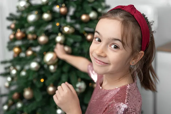 A little girl decorates a Christmas tree, hangs balls. — Stock Photo, Image