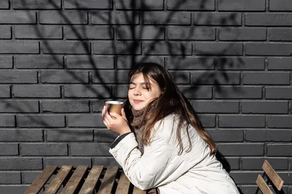 Junge Frau genießt einen Drink an der Backsteinmauer des Cafés. — Stockfoto